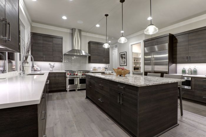 A modern kitchen interior with stainless steel accessories, dark wood cabinets, white countertops, and multiple pendant lights. soft lighting enhances the room's elegant ambiance.